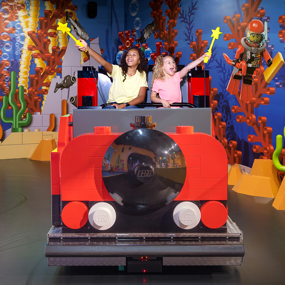 Two children enjoying a ride at the LEGO Discovery Center, interacting with LEGO-themed underwater scenery using wands.