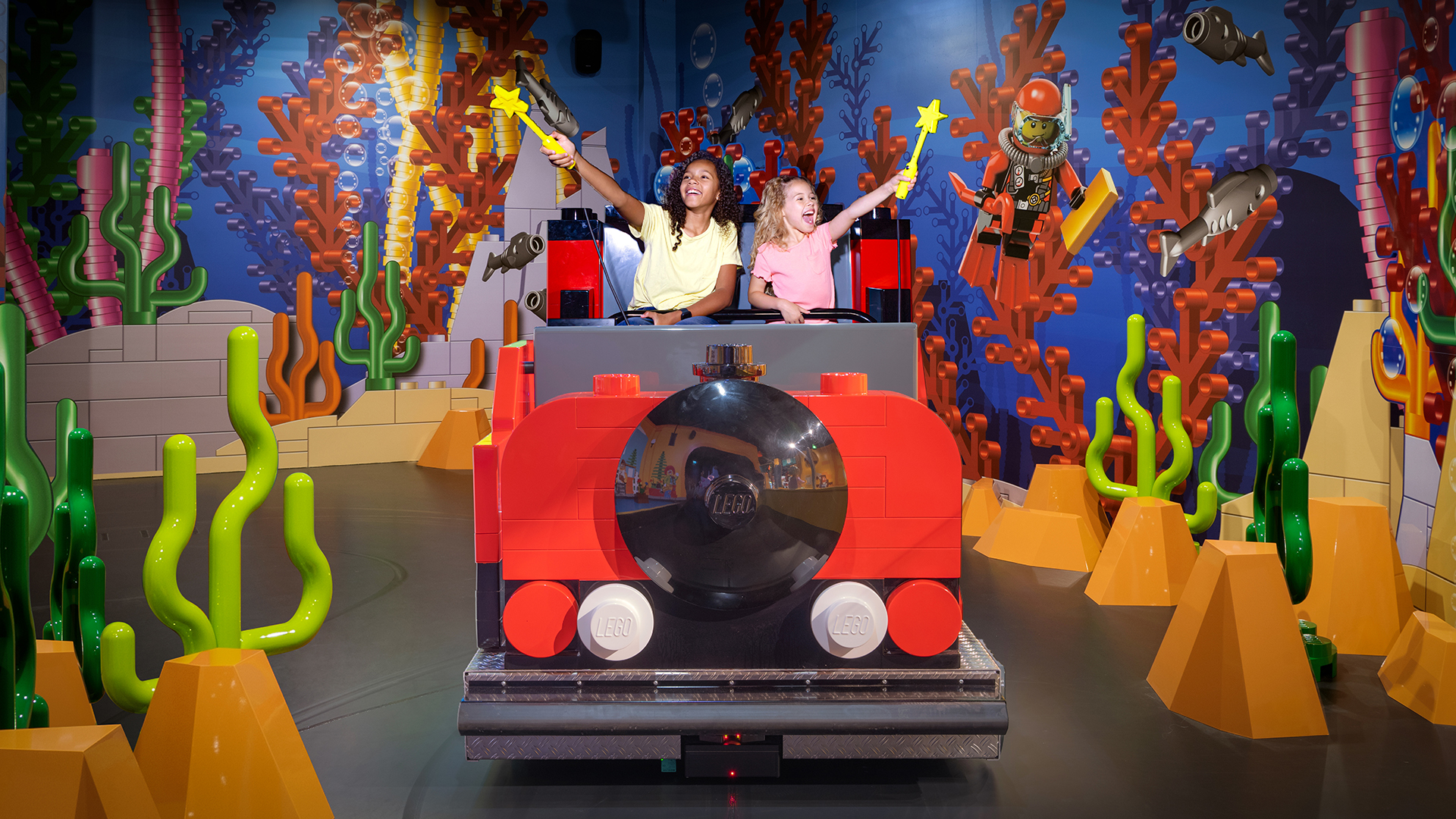 Two children enjoying a ride at the LEGO Discovery Center, interacting with LEGO-themed underwater scenery using wands.