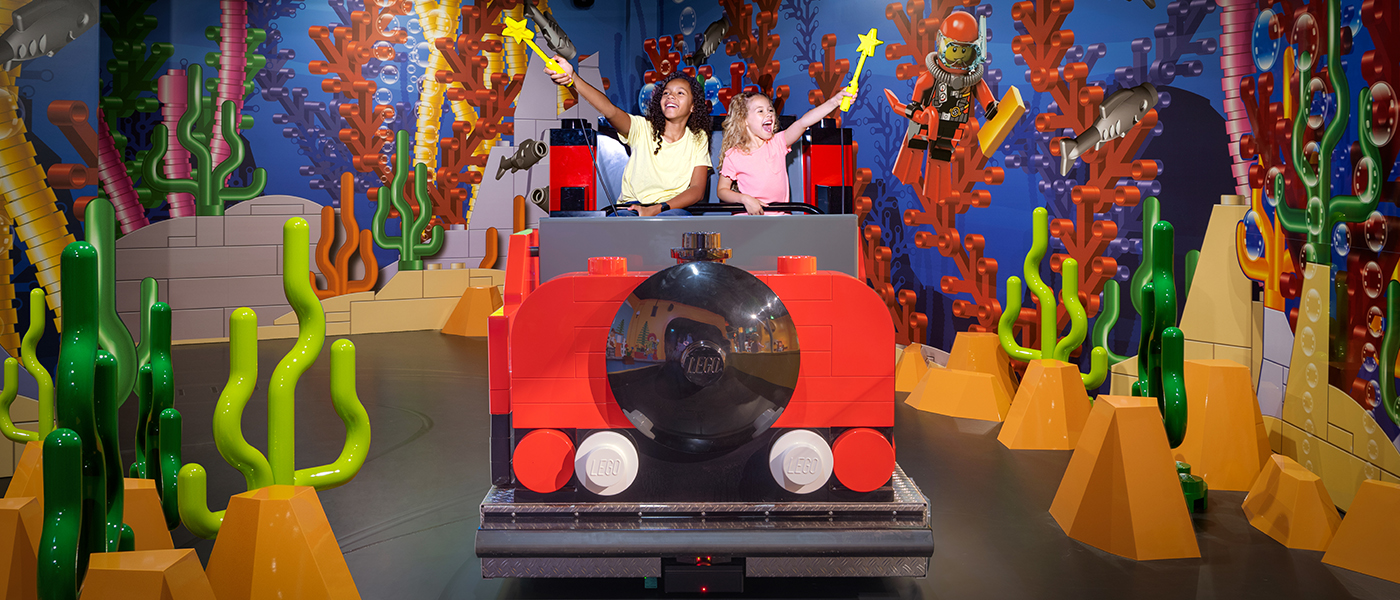 Two children enjoying a ride at the LEGO Discovery Center, interacting with LEGO-themed underwater scenery using wands.